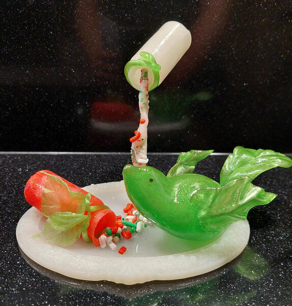 Suikerkunstwerk in een kerst thema met een blauwe vogel en daarnaast een flesje dat vliegt en snoep naar beneden giet.