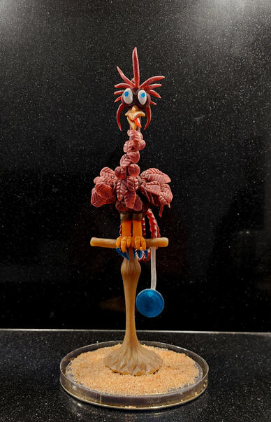 Suikerkunstwerk van een paarse vogel die op een stokje zit en een gek gezicht trekt.