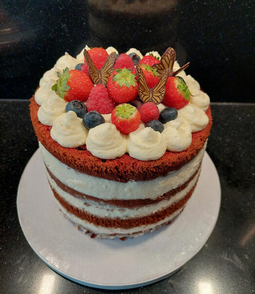 Red velvet cake met vier lagen. De bovenkant is gedecoreerd met aardbeien, frambozen, zwarte bessen en vlinders gemaakt van chocolade.